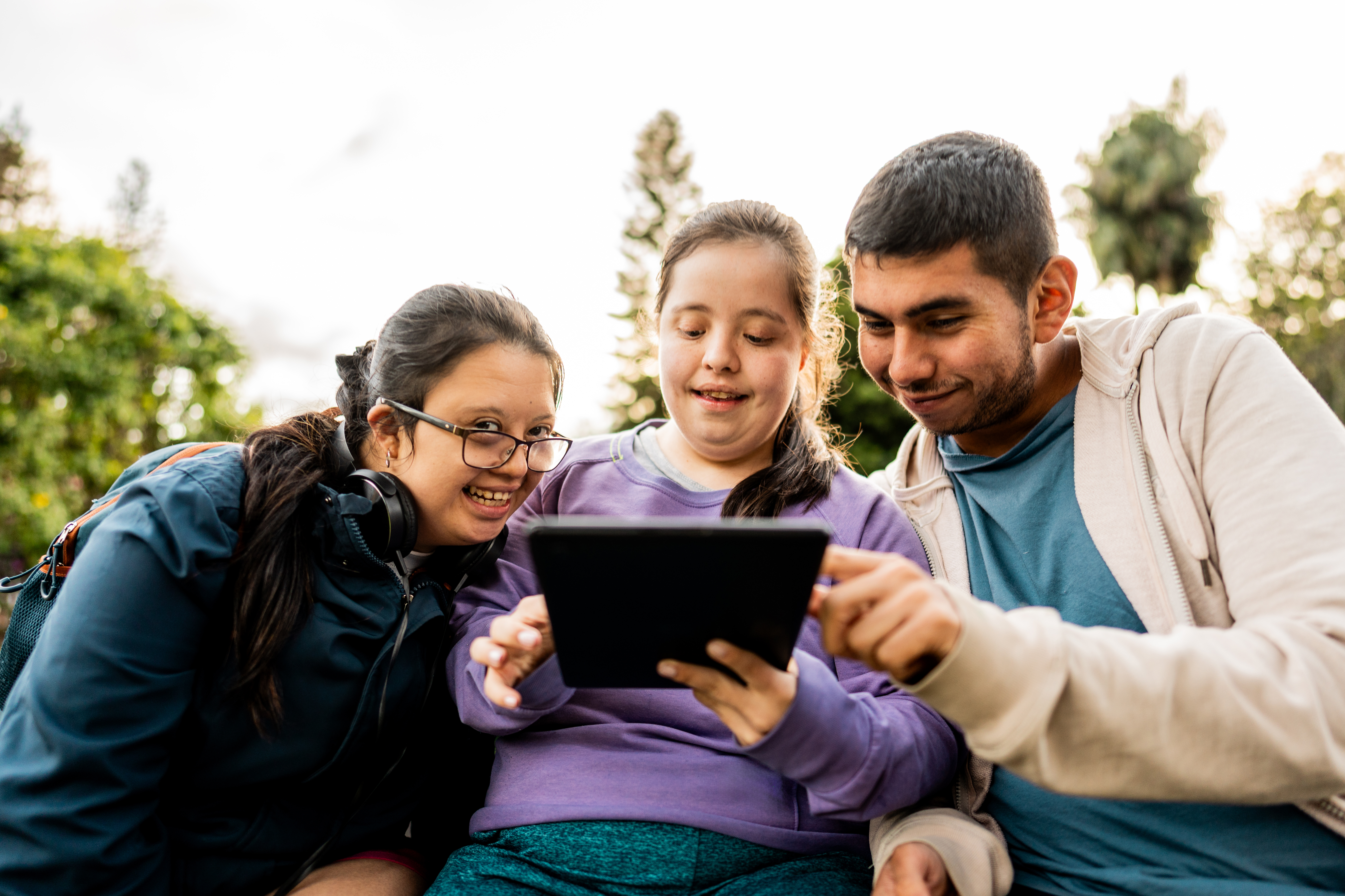Three young people with disabilities smiling together as they look at a tablet
