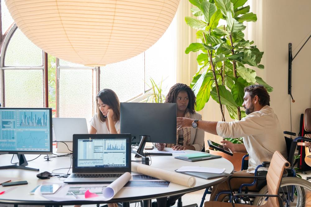 A designer, an accessibility lead, and a developer who uses a wheelchair reviewing data and design mockups together at a shared desk